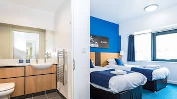 A modern hotel room with a bathroom, two beds, a large window, and a motivational quote on the wall.