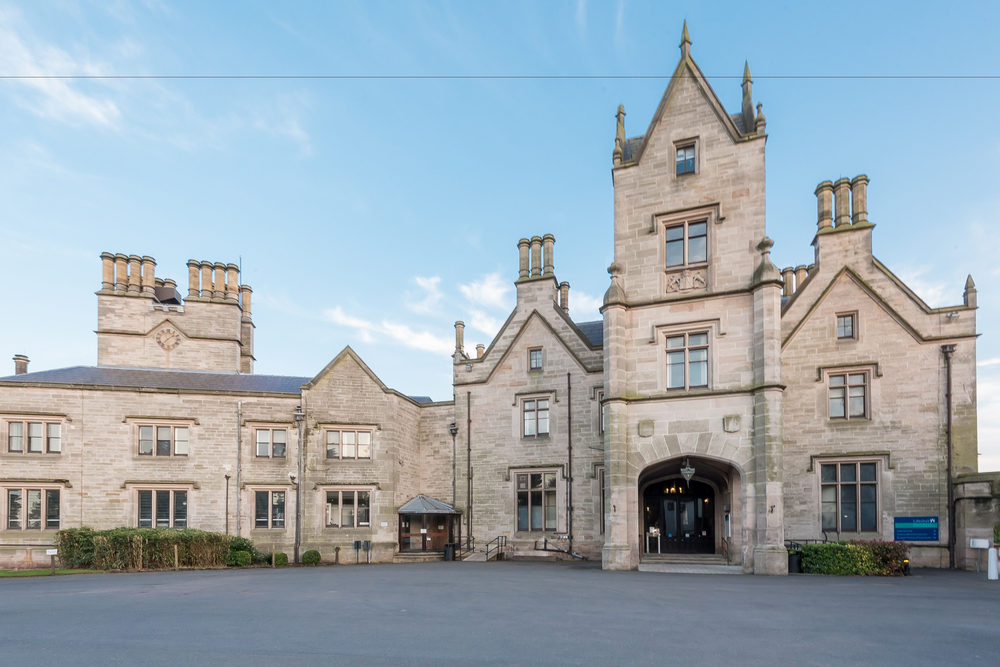 A large, historic stone building with multiple chimneys, a prominent tower, and a central entrance.