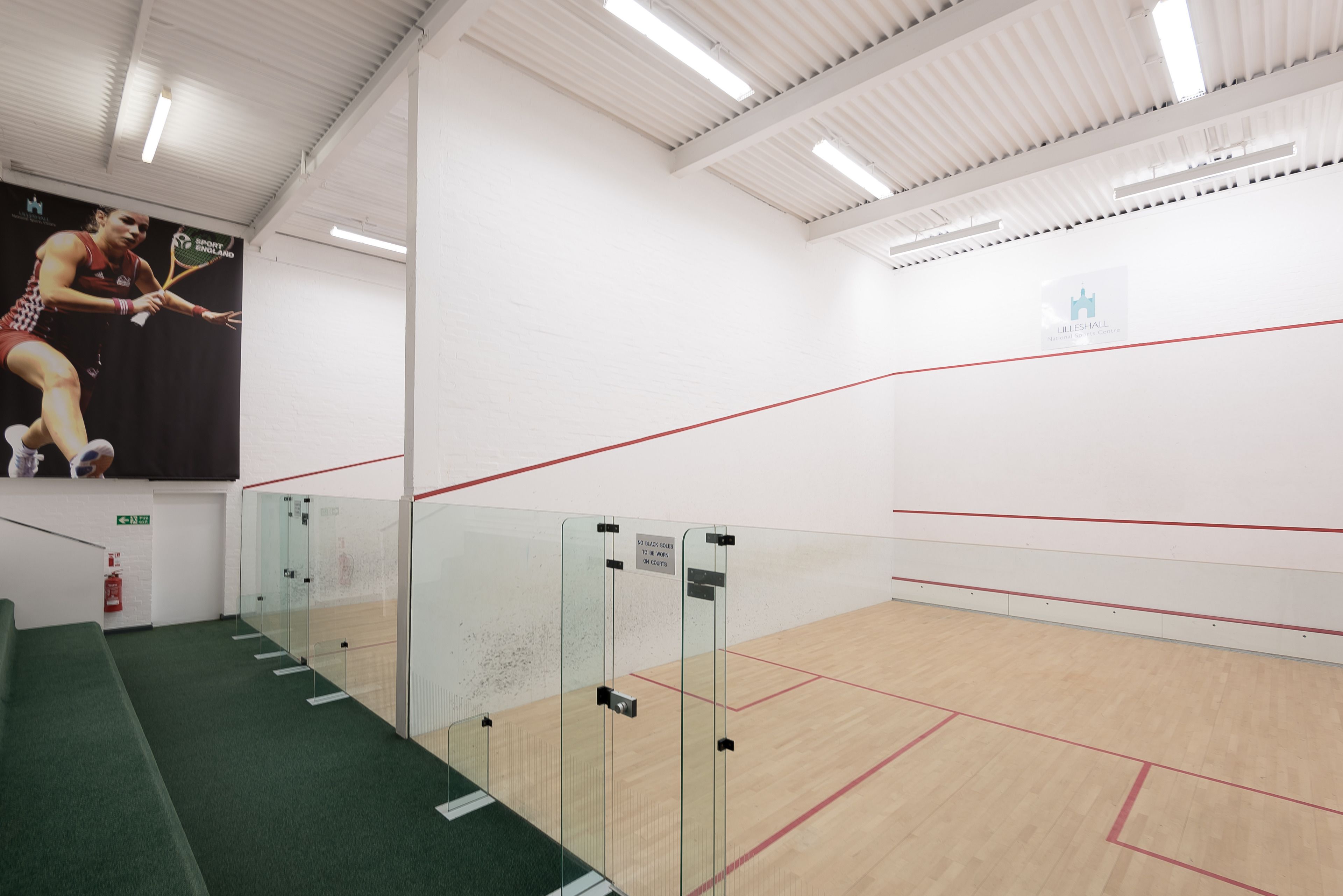 A squash court with glass doors, a wooden floor, and a red line marking the court.