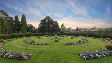 Un jardín formal con una estatua central, setos cuidadosamente recortados y una variedad de plantas en flor.