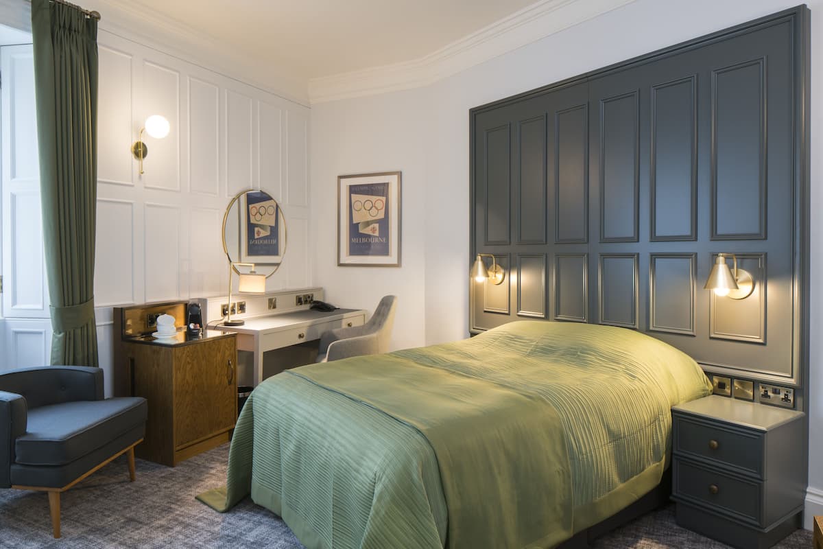 A hotel room with a bed, a desk, a chair, and a nightstand.