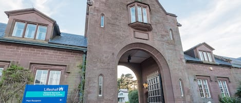 A historic building with an arched entrance, a sign indicating it is the National Sports & Conference Centre, and a lion statue at the entrance.