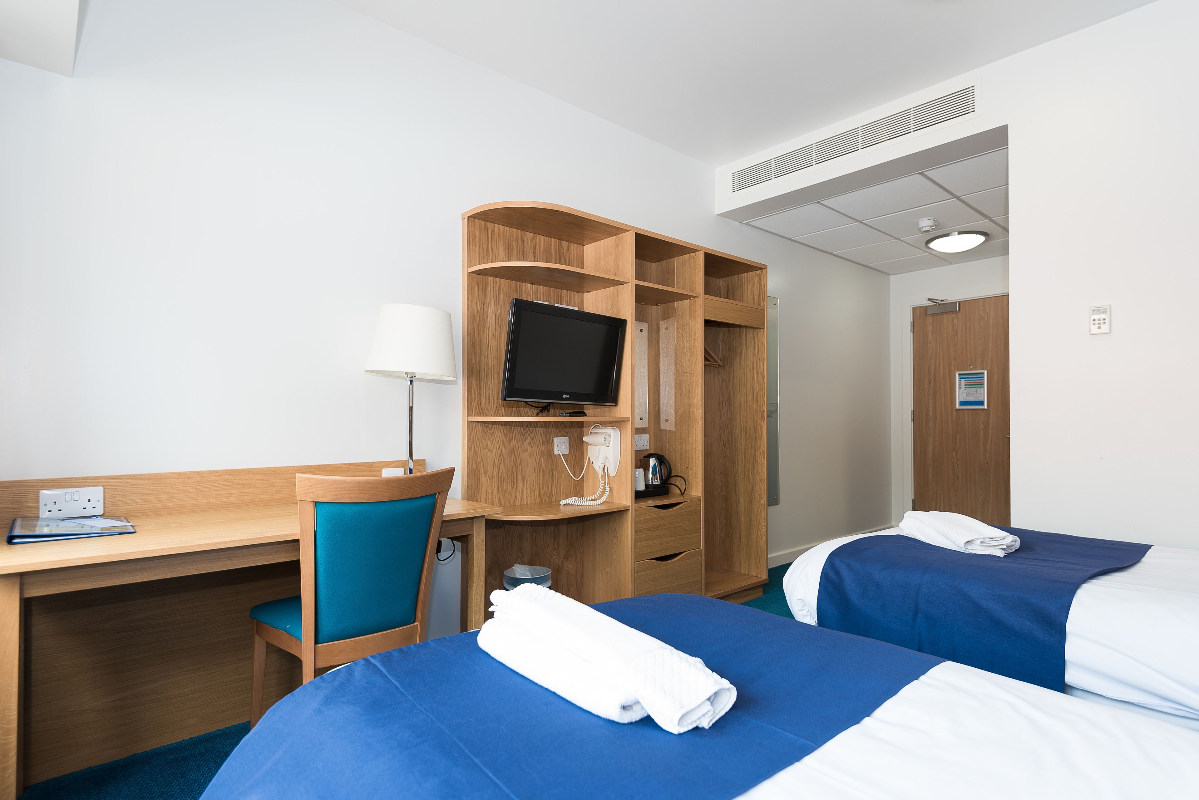 A hotel room with two beds, a desk with a chair, a TV, and a wardrobe.