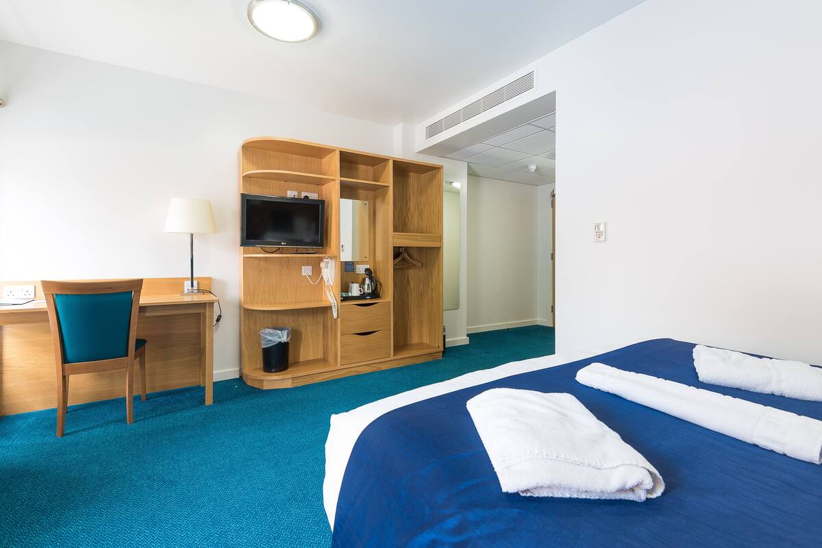 A hotel room with a bed, a desk, a TV, and a wardrobe.