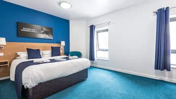 A hotel room with a large bed, a headboard, a nightstand, a lamp, a window with curtains, and a motivational quote on the wall.