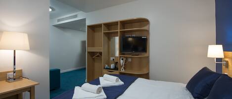 Habitación de hotel con cama, dos mesitas de noche con lámparas, televisión, armario de madera y alfombra azul.