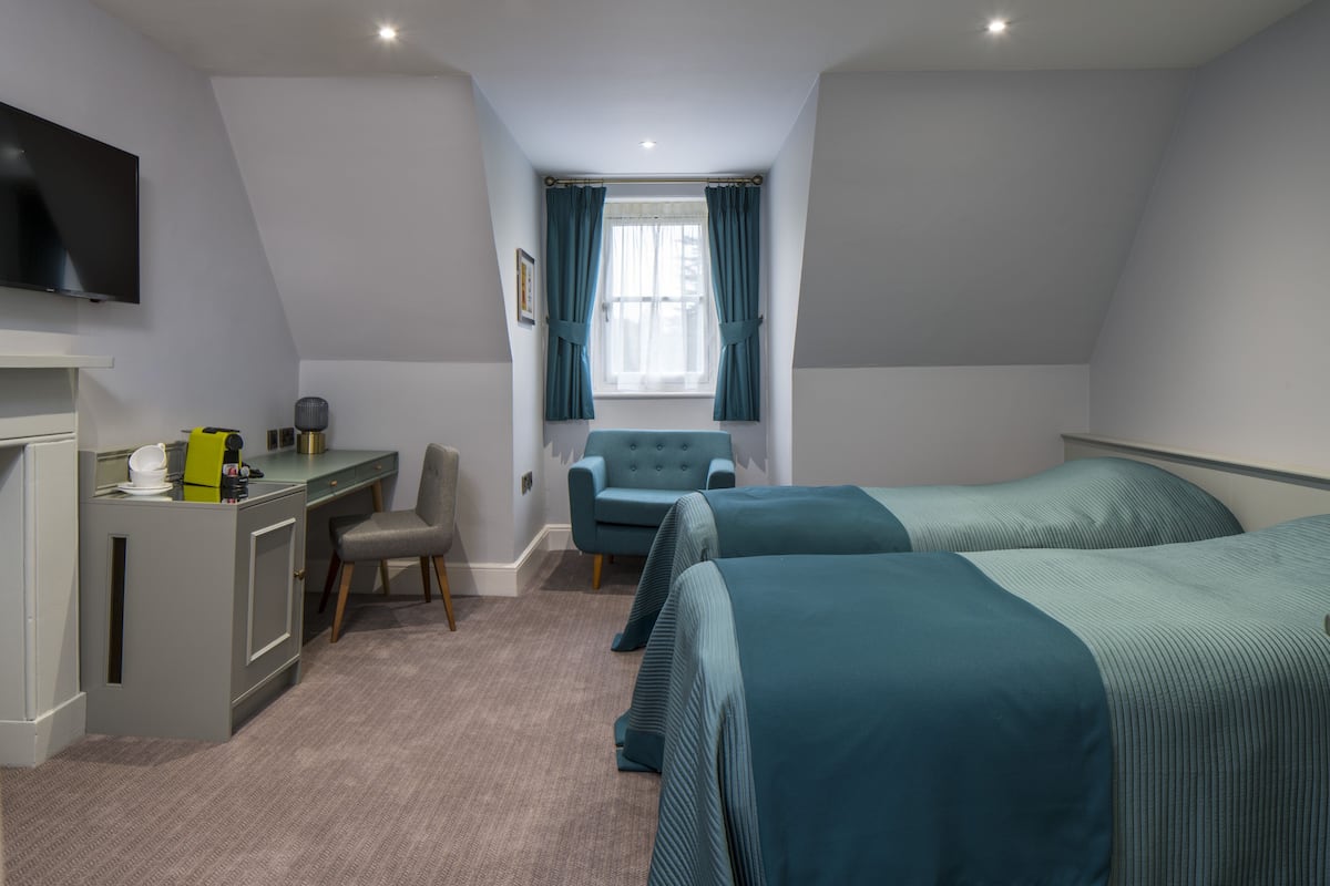 A hotel room with a desk, two beds, a chair, and a TV.