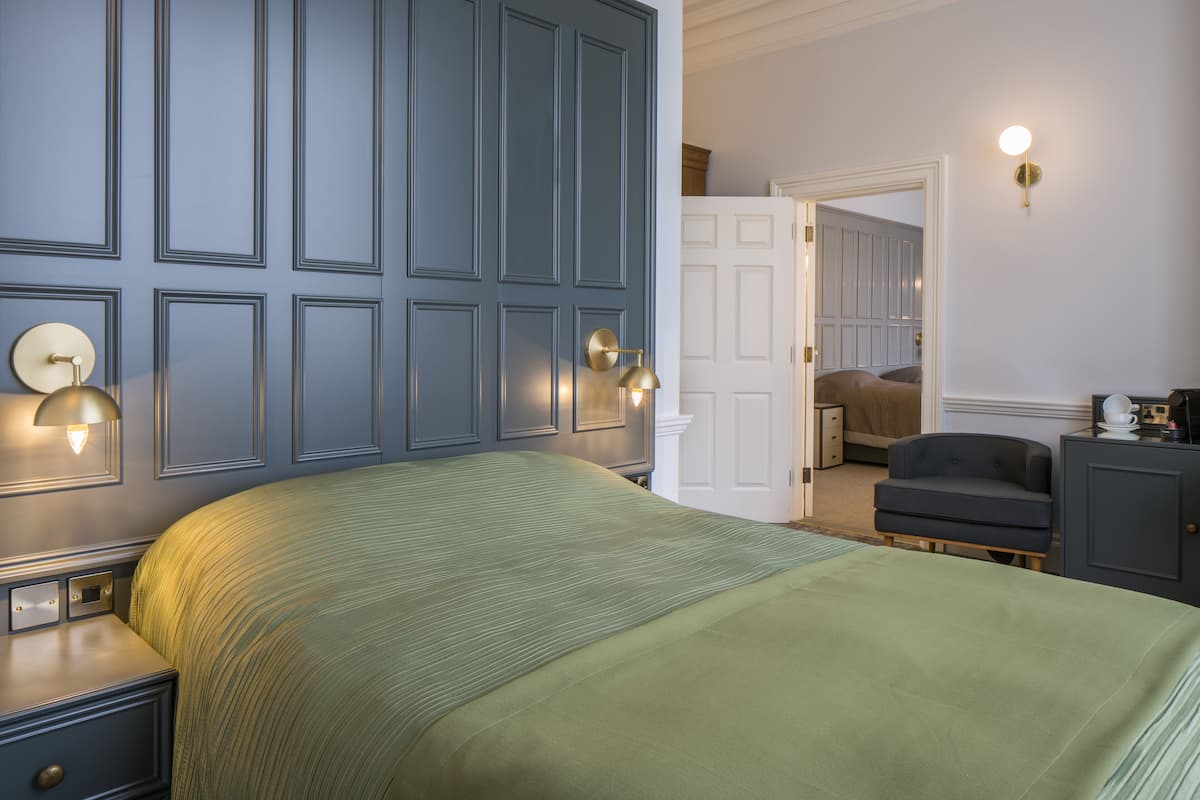 A bedroom with a large bed, a nightstand, a dresser, and a wall-mounted lamp.