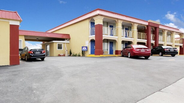 A motel with a red and yellow facade, a covered parking area, and a blue entrance door.