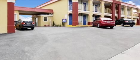 A motel with a red and yellow facade, a covered parking area, and a blue entrance door.