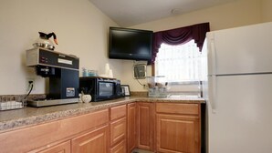 A compact kitchen with wooden cabinets, a Bunn coffee maker, a microwave, a toaster, and a refrigerator.