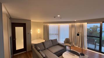 A modern living room with a sofa, armchair, and coffee table, large windows with curtains, and a view of the outdoors.