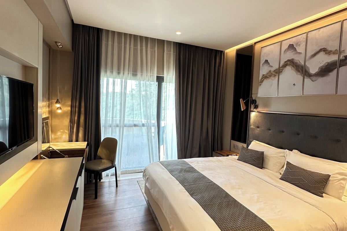 A modern hotel room with a large bed, a desk, a chair, and a television.