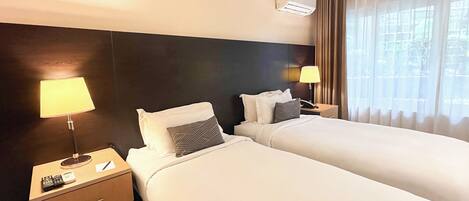 Habitación de hotel con dos camas, una mesita de noche con lámpara, teléfono y control remoto.