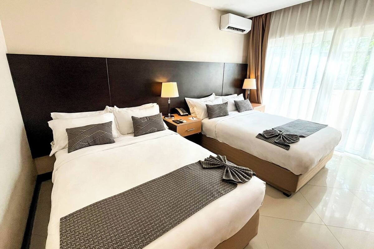 A hotel room with two beds, a nightstand with a lamp, and an air conditioning unit.