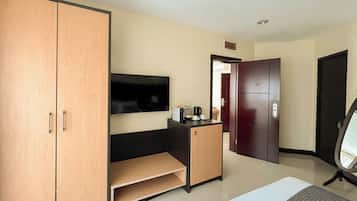 Hotelkamer met een grote kast, een klein bureau met een flatscreen televisie, een koffiezetapparaat en een deur naar een andere kamer.