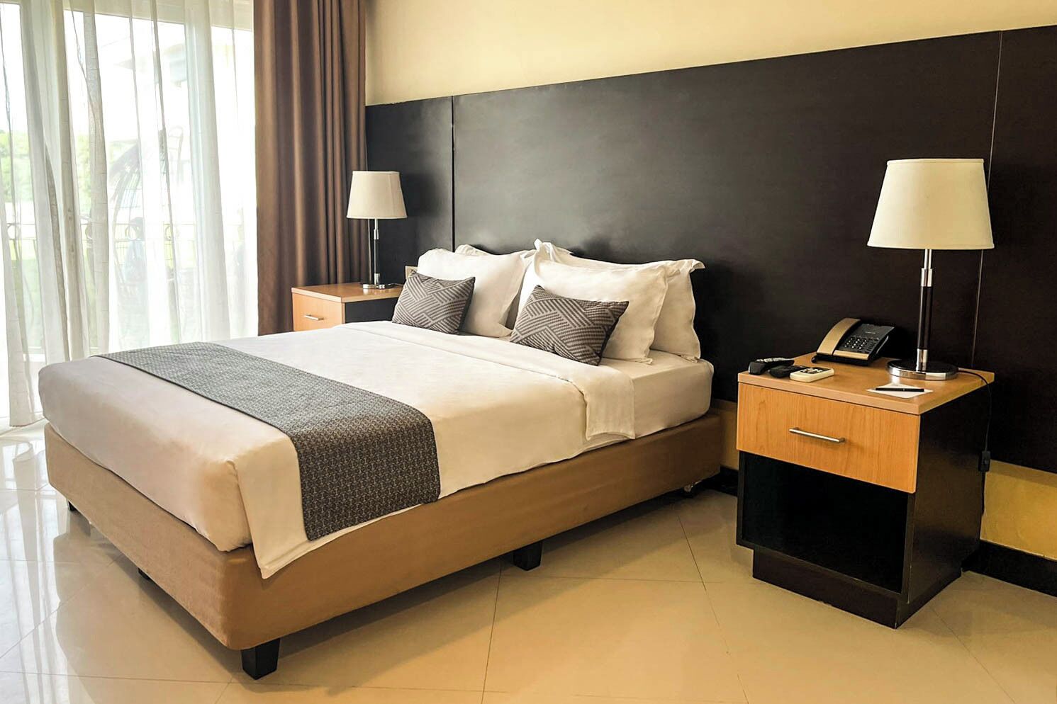 A hotel room with a large bed, two bedside tables with lamps, a telephone, and a nightstand.