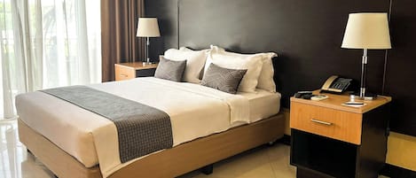 A hotel room with a large bed, two bedside tables with lamps, a telephone, and a nightstand.