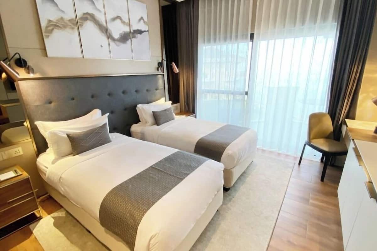 A hotel room with two beds, a desk, a chair, and a large window with curtains.