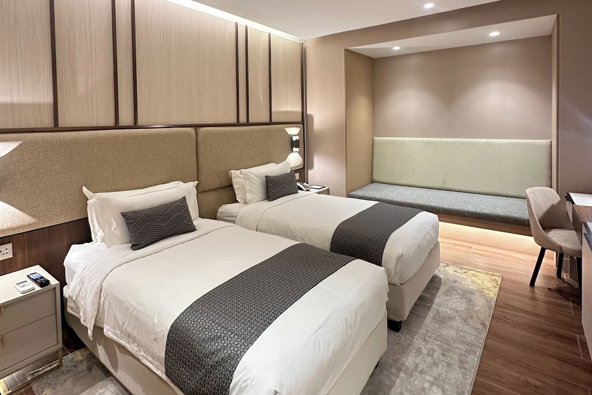 A modern hotel room with two beds, a desk, and a seating area.