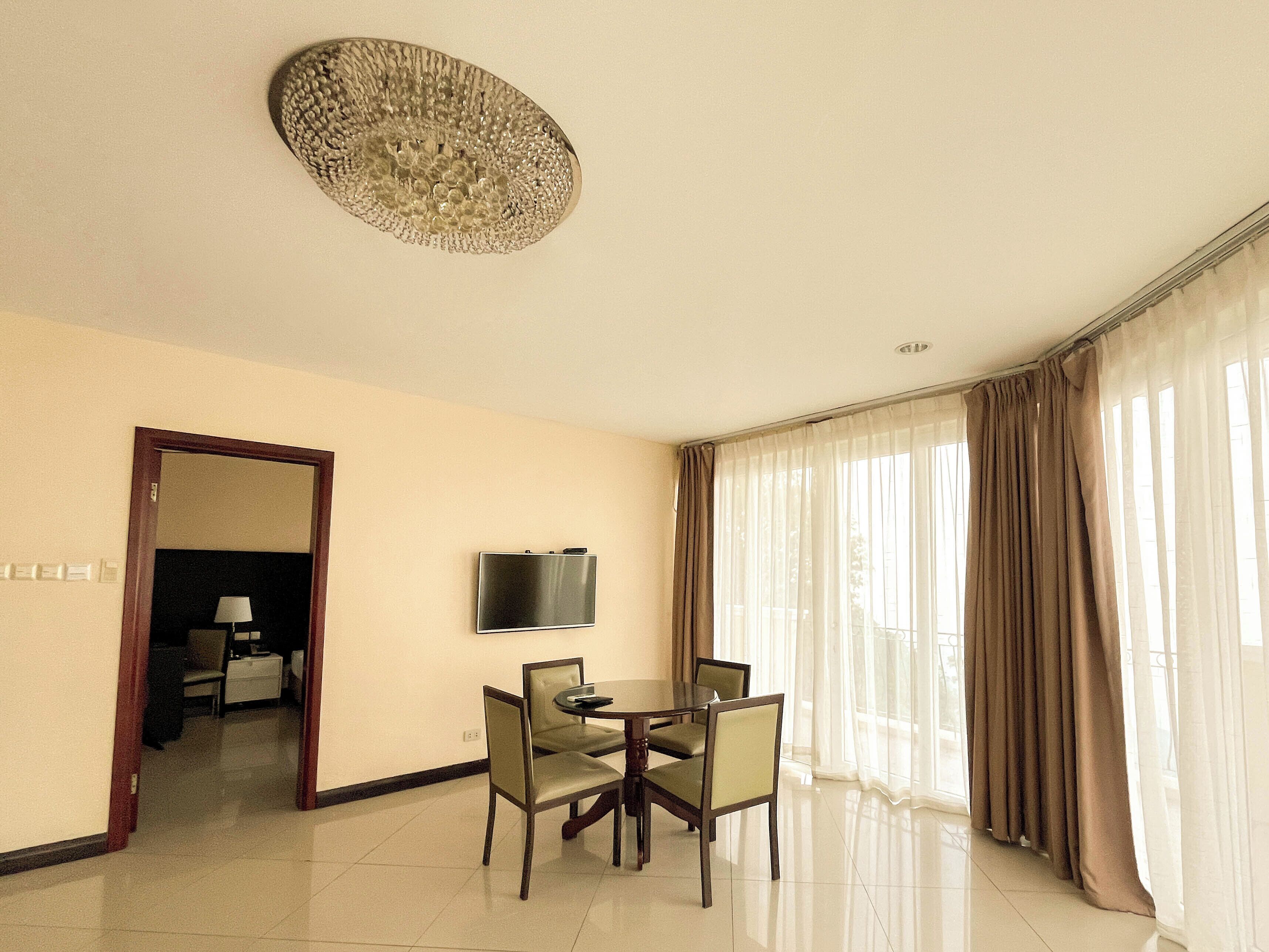 A hotel room with a dining area, a television mounted on the wall, and a view through large windows.