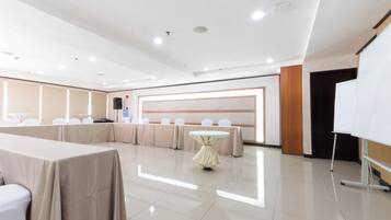 Un salón de conferencias con una mesa larga, mesas redondas más pequeñas y una pizarra.