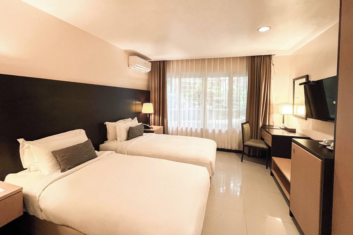 A hotel room with two beds, a desk, a chair, a television, and a window with curtains.