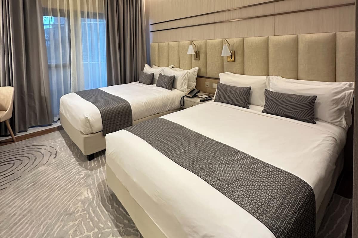 A hotel room with two beds, a desk, a chair, and a large window with curtains.