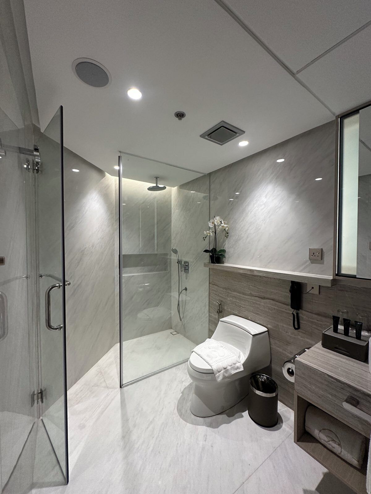 Une salle de bain moderne avec une douche à parois de verre, des toilettes, un meuble-lavabo avec un miroir et une poubelle.