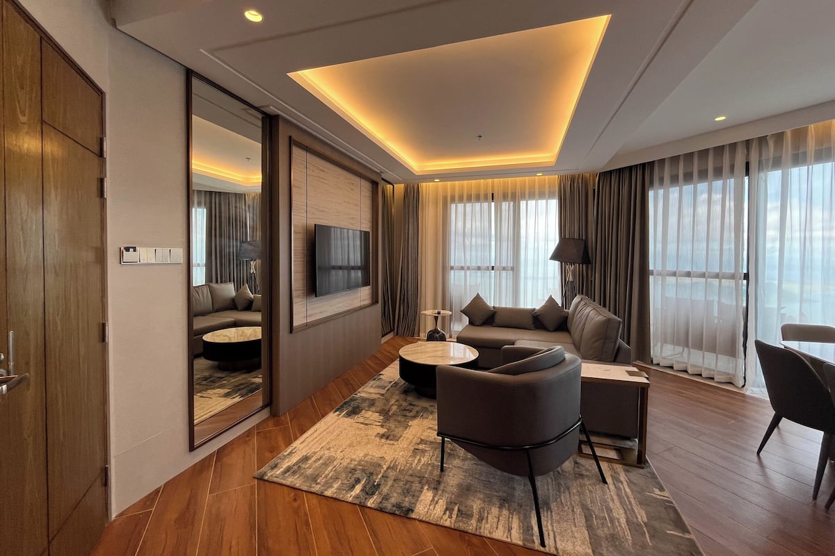 A modern hotel room with a large flat-screen TV, a sofa, a coffee table, and a dining area.