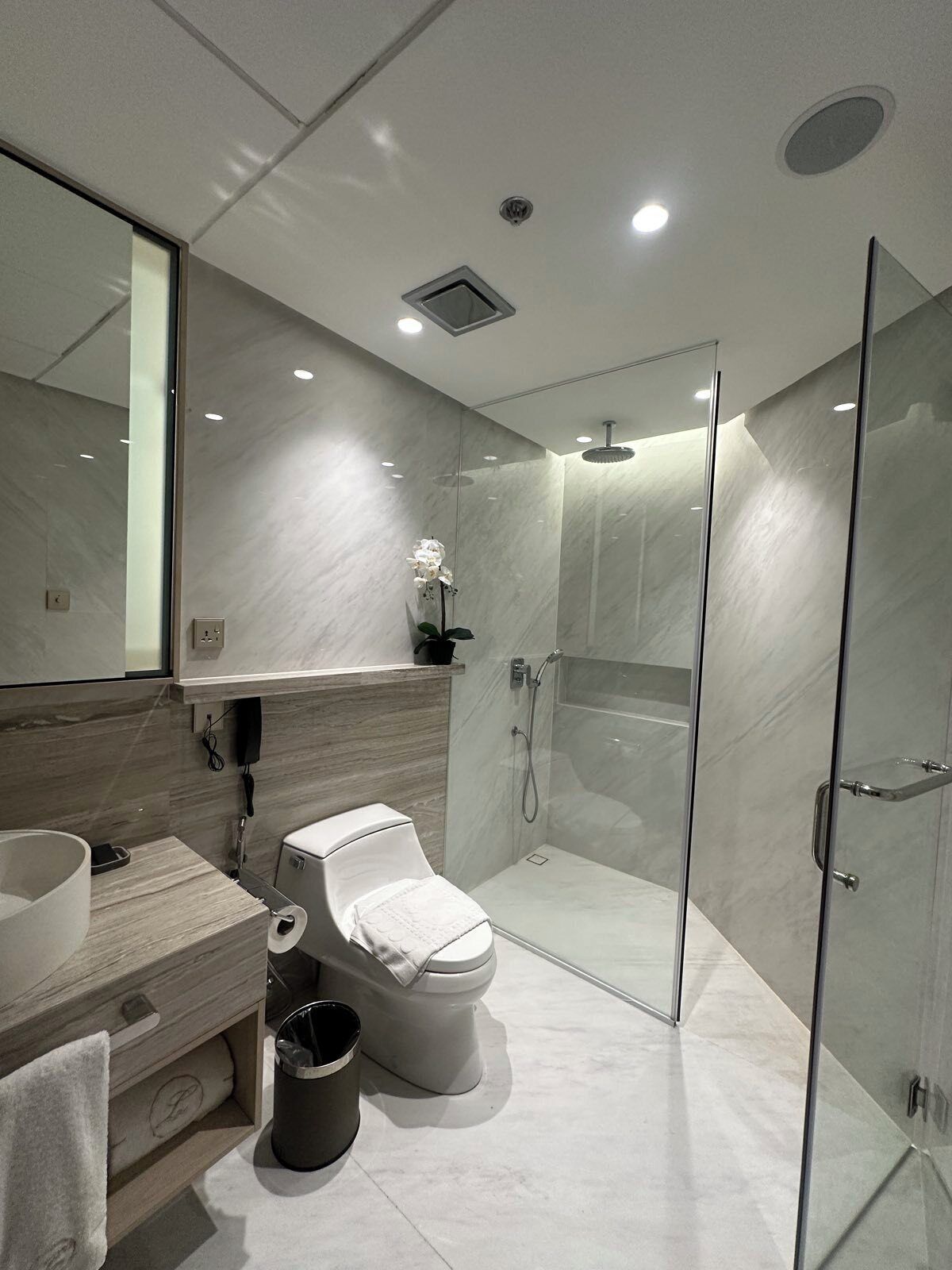 A modern bathroom with a toilet, bidet, glass shower enclosure, and a marble-tiled floor.