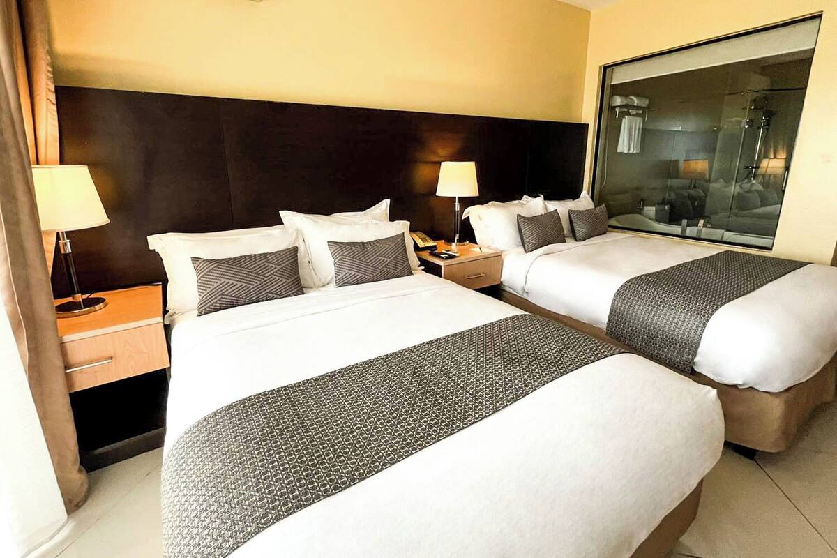 A hotel room with two beds, a large mirror, and a nightstand with a lamp.