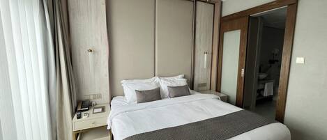 Una habitación de hotel con una cama grande, una mesita de noche con teléfono y un armario.
