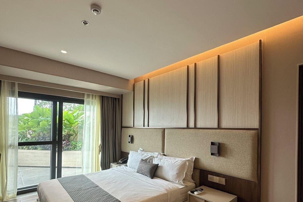 A modern bedroom with a large bed, a bedside table, a nightstand, and a sliding glass door leading to an outdoor area.