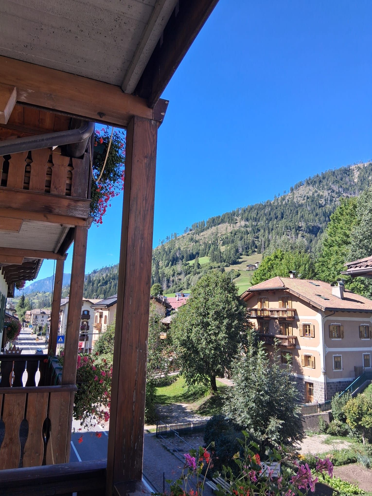 A wooden balcony with a view of a hillside village and a clear blue sky.