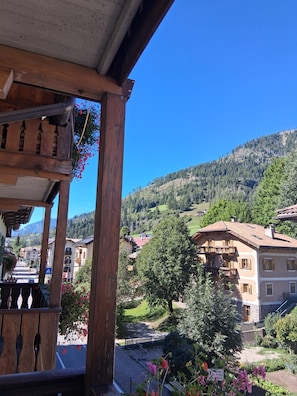 A wooden balcony with a view of a hillside village and a clear blue sky. - Laurino (Moena)