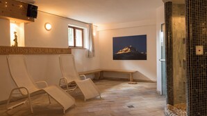 Un cuarto de spa con tres sillones reclinables, un banco de madera, un televisor montado en la pared, una ventana con cortinas y un cuadro grande enmarcados de una montaña.