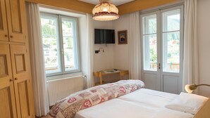 Un dormitorio con cama, escritorio, televisor y ventanas amplias.