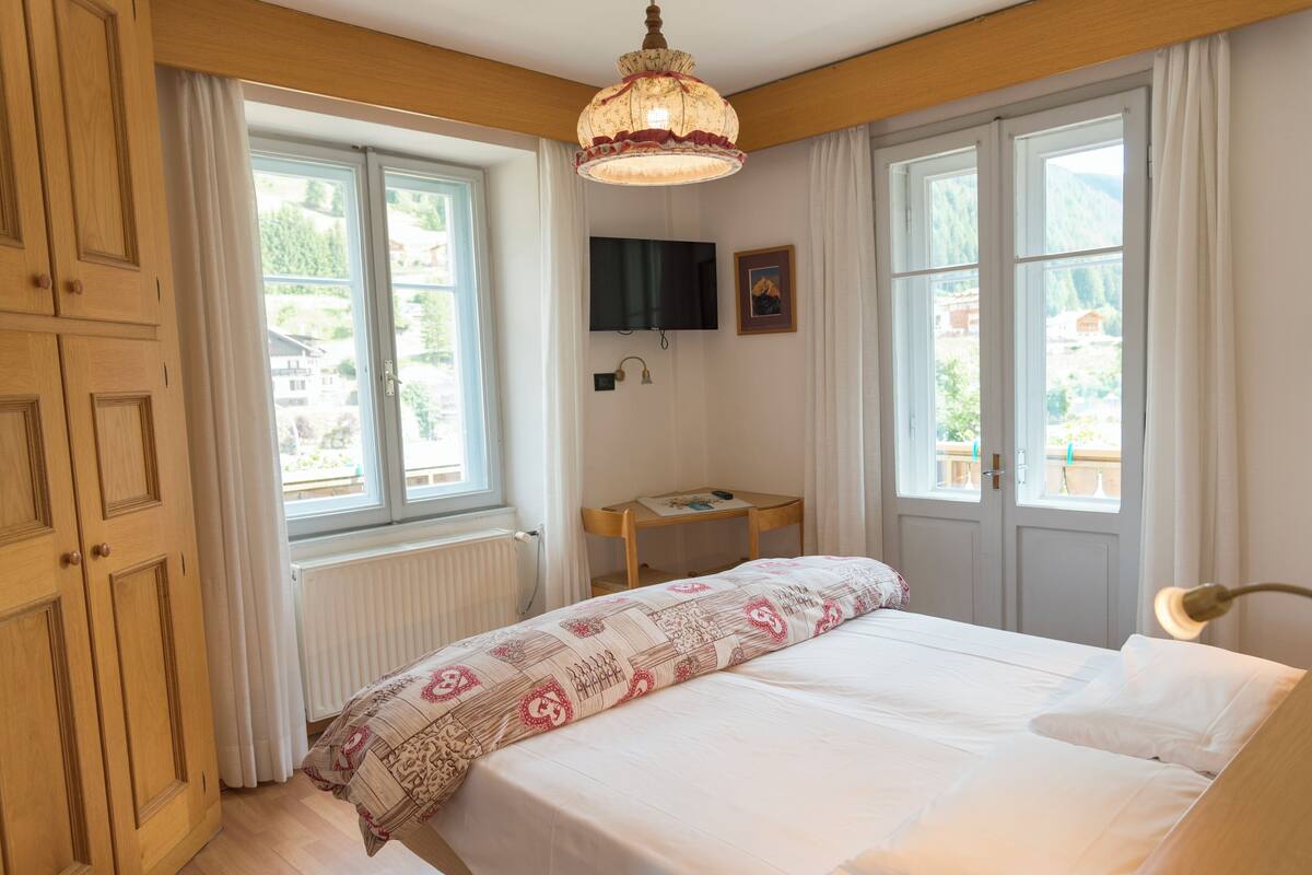 Ein Schlafzimmer mit einem Bett, einem Schreibtisch, einem Fernseher und großen Fenstern.
