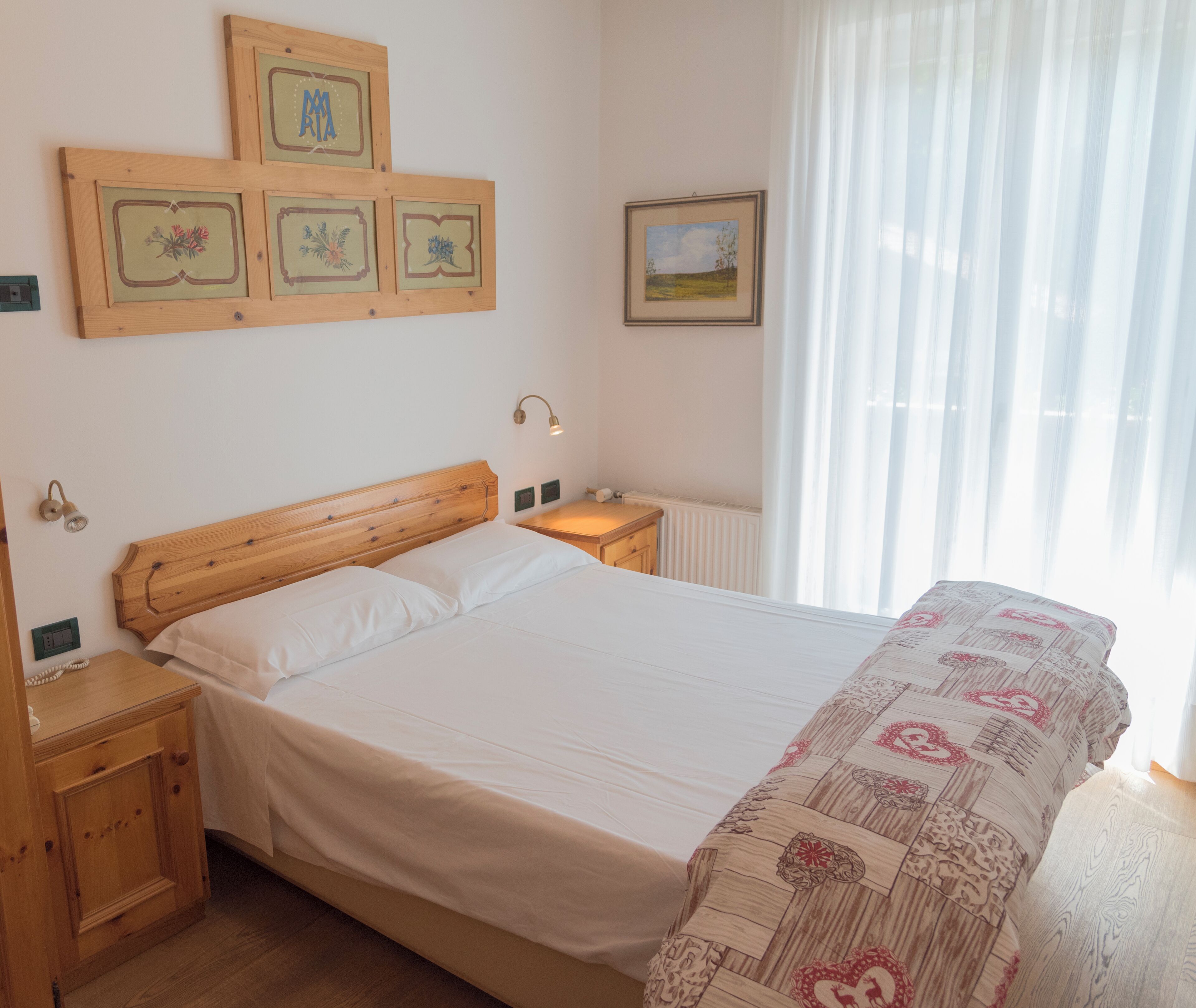 Un dormitorio con cama de madera, mesita de noche y cortinas traslúcidas en la ventana.