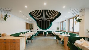 Un restaurante moderno con techo verde curvo central, asientos tapizados en verde y una barra de madera.
