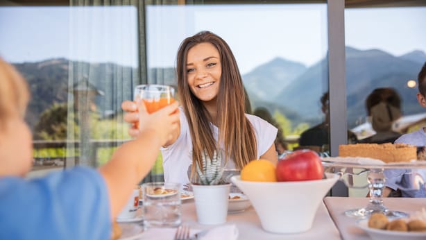 Una mesa de comedor con mantel blanco, un cuenco de fruta y un vaso de jugo de naranja.