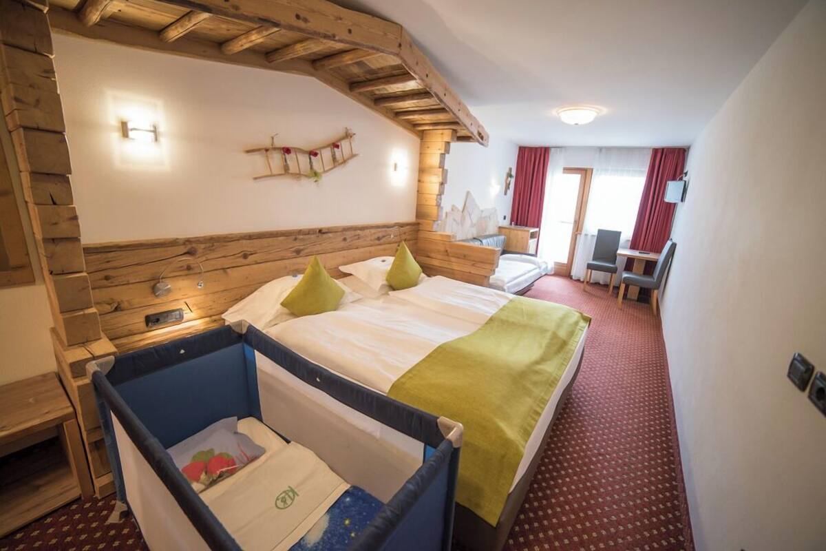 A hotel room with a wooden headboard, a bed with green and white bedding, a small desk with a chair, and a red carpeted floor.