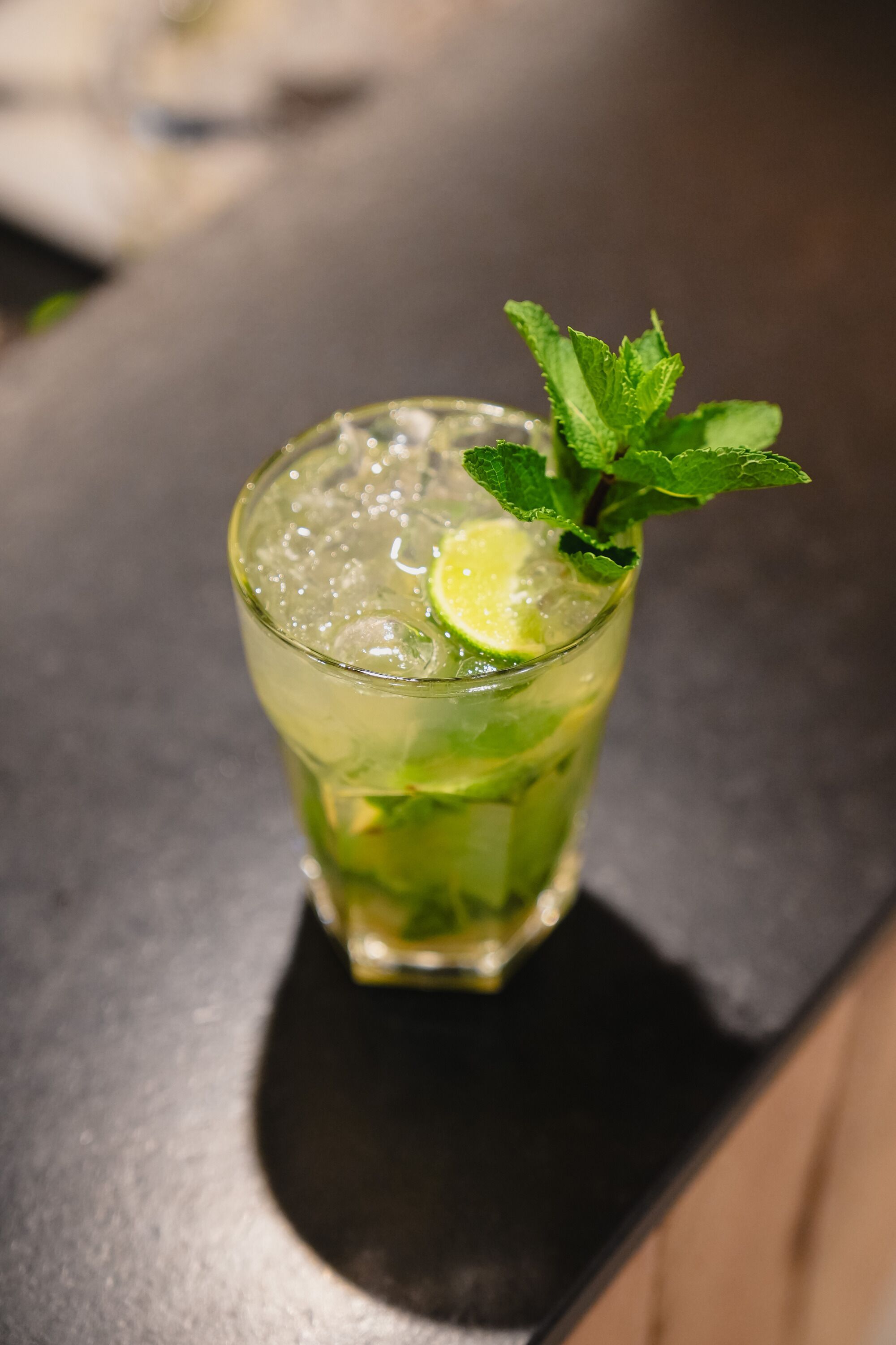 Un grand verre contenant une tranche de citron vert et quelques feuilles de menthe, posé sur le comptoir d’un bar.