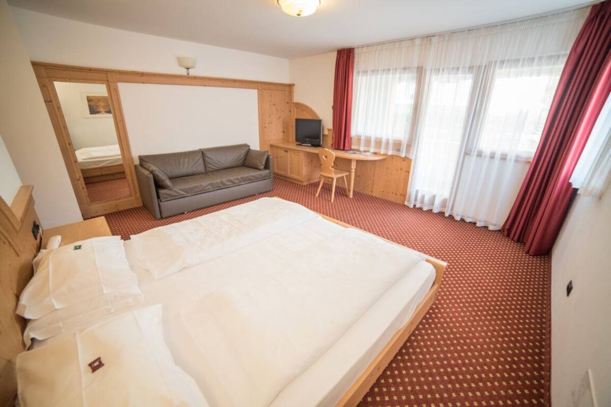 A hotel room with a large bed, a sofa, a desk, and a television.