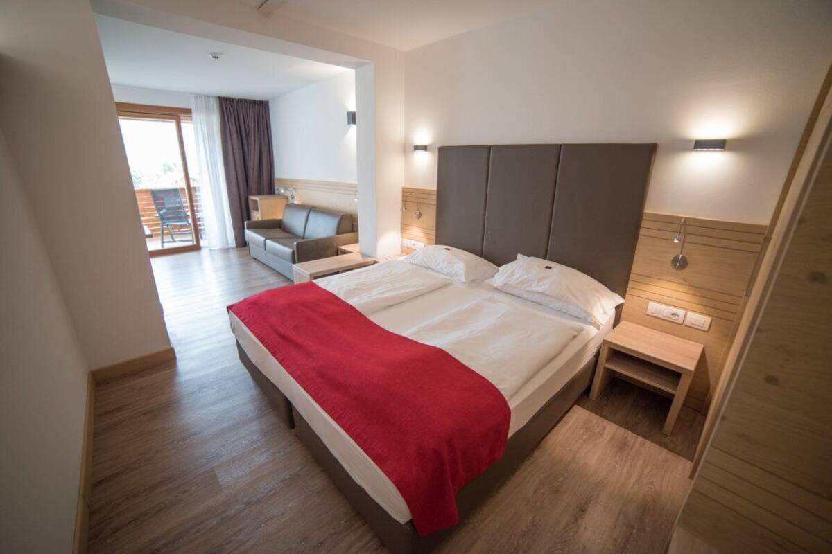 A modern hotel room with a large bed, a wooden headboard, a bedside table, and a view of the outdoor area.