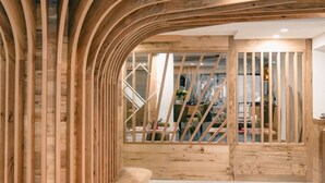 Interior de madera con vigas curvas, una escalera y vista a otra habitación.