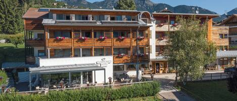 A hotel with a restaurant patio, wooden balconies with flower boxes, and a mountain backdrop.