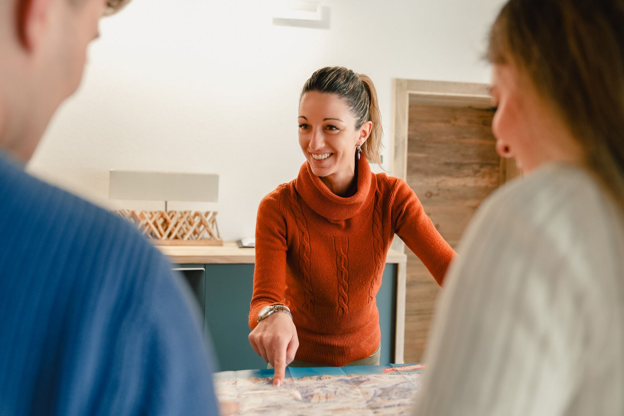 A person in an orange sweater pointing at a map on a table.