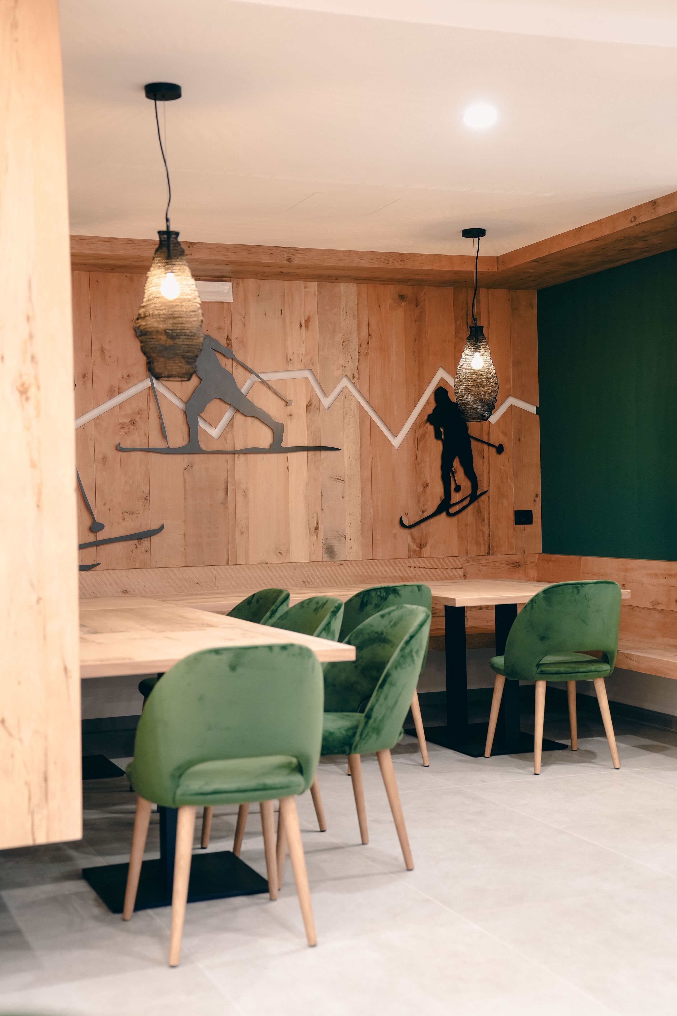 Un espace repas avec des murs en bois, des chaises recouvertes d’un tissu vert et des luminaires suspendus.